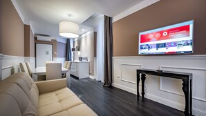 Una habitación de hotel moderna con una televisión de pantalla plana grande, un sofá, un área de comedor y un pasillo.