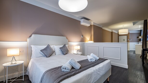 Habitación de hotel moderna con una cama grande, lámparas de noche, una lámpara de techo redonda y un baño visible al fondo.