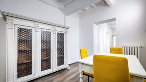 A dining area with a white table and yellow chairs, a white cabinet with decorative glass doors, and a radiator on the wall. - YiD quiet 2BR apartment with private garden (Florencia)
