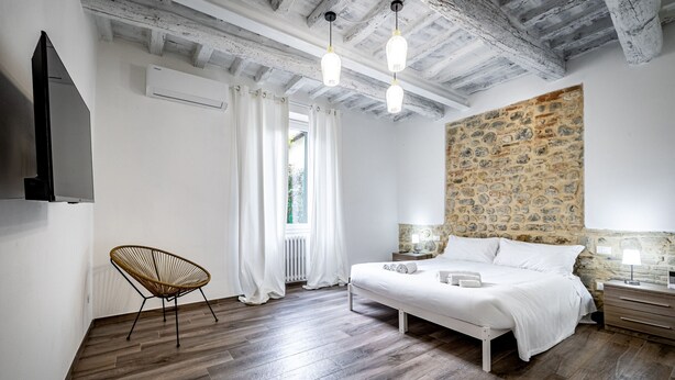 A bedroom with a wooden floor, a bed, a chair, a stone wall, and a ceiling with exposed beams. - YiD quiet 2BR apartment with private garden (Florencia)