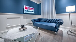 A modern living room with a blue sofa, a glass coffee table, a flat-screen TV mounted on the wall, and a floor lamp. - Garibaldi Palace The Blue Charme (Prato)