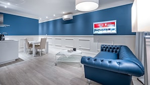 A modern living room with a blue sofa, a glass coffee table, a white dining table, and a kitchen area. - Garibaldi Palace The Blue Charme (Prato)