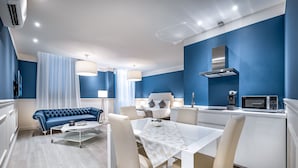 A modern hotel room with a dining area, a sofa, a kitchen, and a large window with curtains. - Garibaldi Palace The Blue Charme (Prato)
