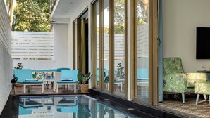 An indoor swimming pool with clear glass walls, blue lounge chairs, and a green sofa. - Nerul Nirvana Nest by Dia Hotels (Nerul)