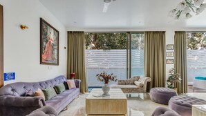 A modern living room with a purple sofa, a beige coffee table, and a large window with curtains. - Nerul Nirvana Nest by Dia Hotels (Nerul)