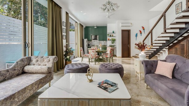 A modern living room with a sofa, ottomans, a coffee table, and a staircase. - Nerul Nirvana Nest by Dia Hotels (Nerul)