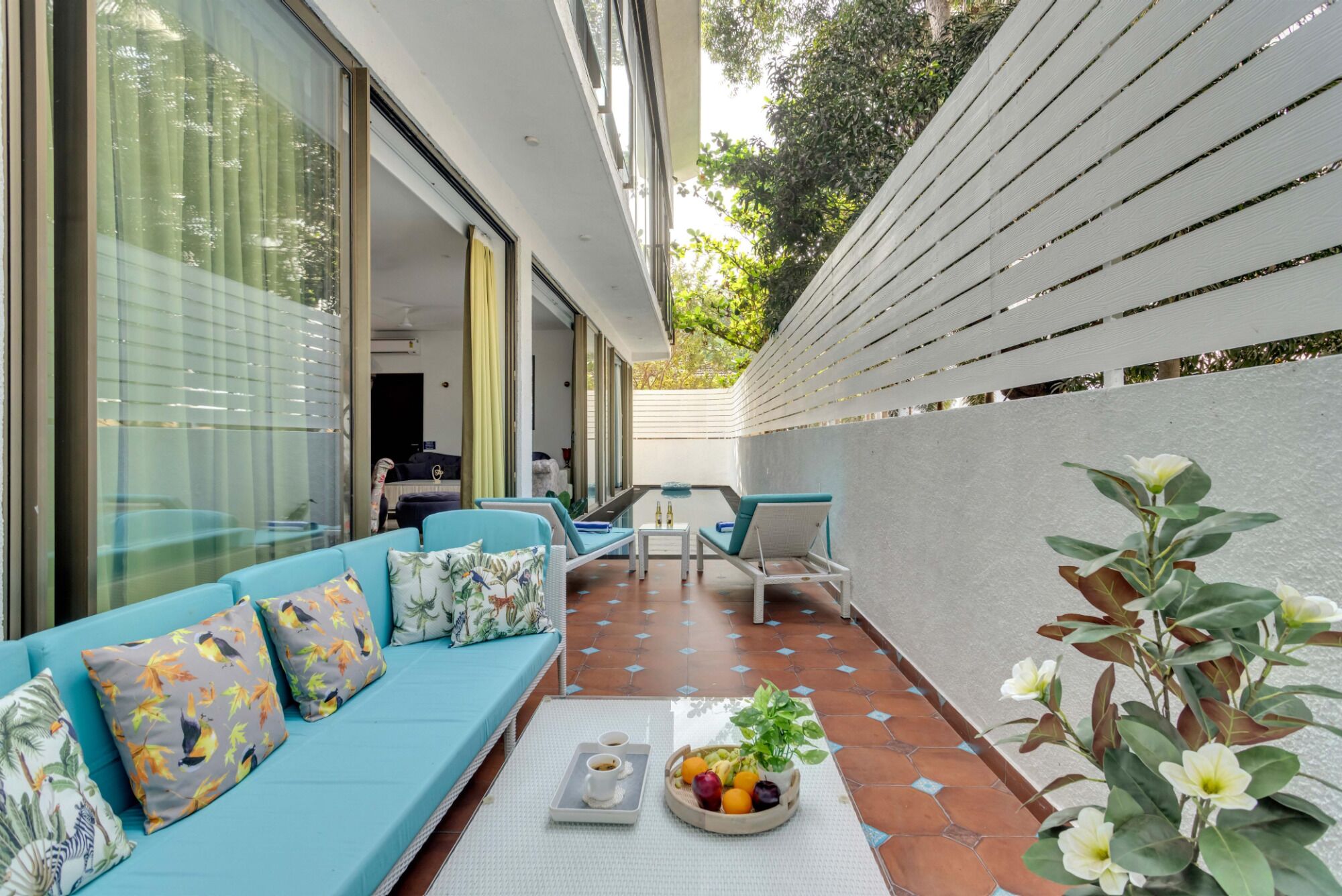 Un patio moderno al aire libre con un sofá azul, una mesa de comedor y una bandeja de frutas y bebidas.