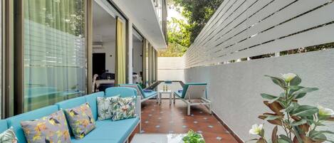 Un patio moderno al aire libre con un sofá azul, una mesa de comedor y una bandeja de frutas y bebidas.