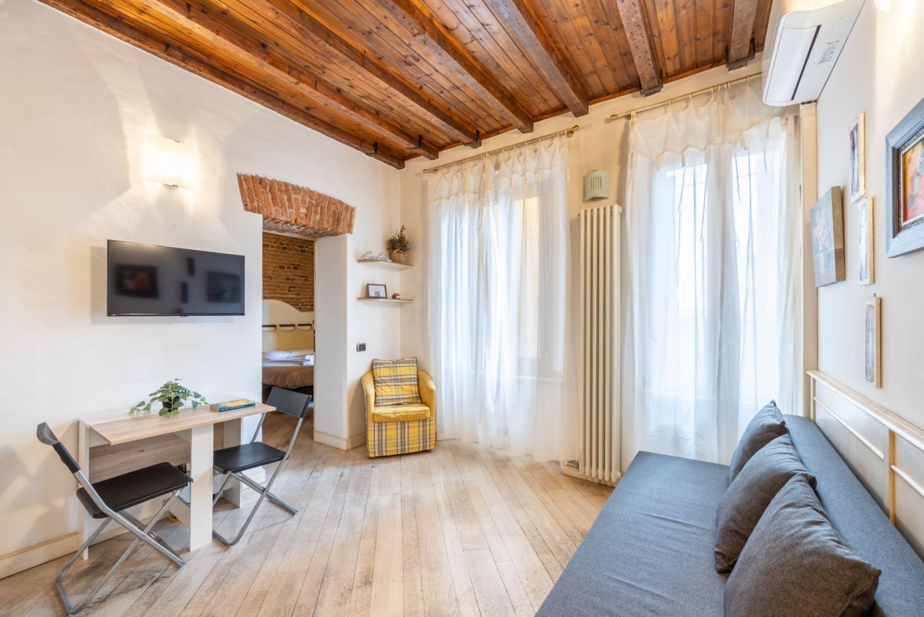 Une pièce chaleureuse avec un plafond en bois, un lit, un canapé, un bureau avec une chaise et un téléviseur fixé au mur.