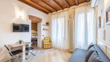 Une pièce chaleureuse avec un plafond en bois, un lit, un canapé, un bureau avec une chaise et un téléviseur fixé au mur.