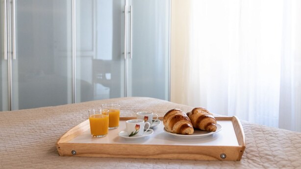 Ett brickbord med croissanter och apelsinjuice står på sängen i ett hotellrum.
