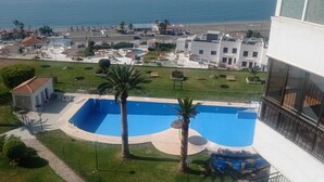 Une piscine bordée de palmiers, une vue sur la plage et un quartier résidentiel en arrière-plan.