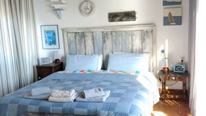 Une chambre avec un plafond en bois, un lit recouvert d’une courtepointe à carreaux bleus et blancs, une tête de lit en bois et une petite table avec une lampe.