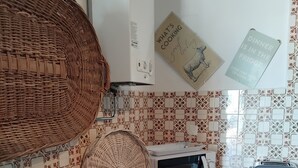 Une cuisine équipée d’un four à micro-ondes, d’un grille-pain et d’un lave-linge. On y trouve des paniers en osier et une bouteille de vin posée sur le comptoir.