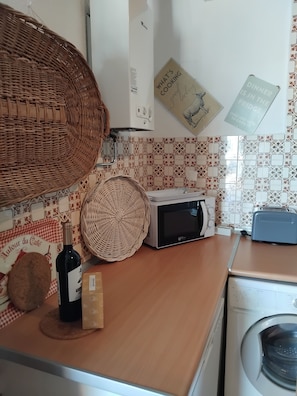 A kitchen with a microwave, toaster, and washing machine. There are wicker baskets and a wine bottle on the counter. - Sea view Penthouse close to beach (El Peñoncillo)