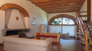 A living room with a fireplace, a sofa, a dining table, and a staircase. - Residence La Canova II (Marina di Grosseto)