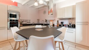 Une cuisine moderne dotée d’un îlot central, de chaises blanches, d’appareils électroménagers en acier inoxydable et d’un luminaire suspendu.