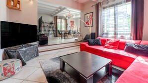 Un salon moderne avec un canapé rouge, un téléviseur à écran plat, une table basse et, au fond, un coin repas.