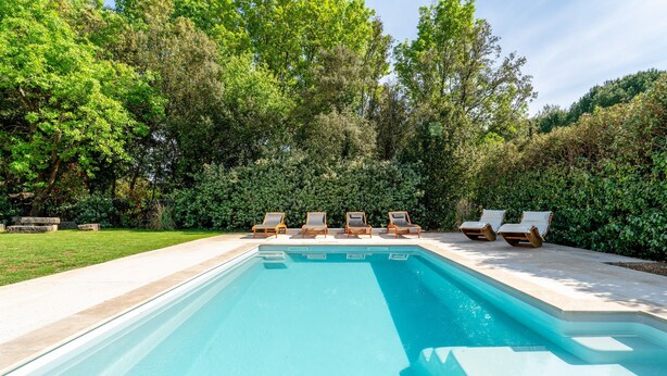 Une piscine rectangulaire dont le bord est recouvert de carreaux, entourée d’une terrasse en béton. Six chaises longues sont alignées le long du bord de la piscine.