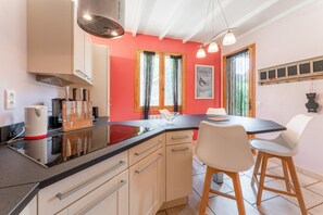 Une cuisine avec un plan de travail noir, des armoires blanches et un mur rouge. On y trouve une fenêtre avec des rideaux, un luminaire suspendu et un tableau encadré accroché au mur.