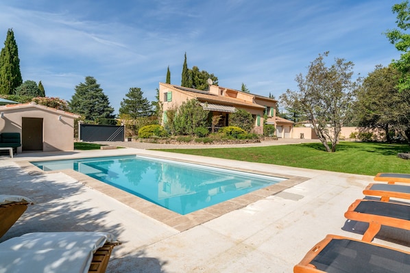 Une piscine avec des chaises longues, une maison avec un toit en tuiles et une pelouse bien entretenue.