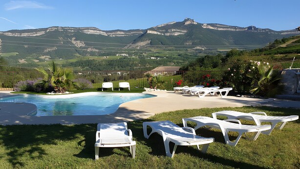 Ein Pool mit Liegestühlen, Blick auf die Berge und ein umzäuntes Grünanlage.