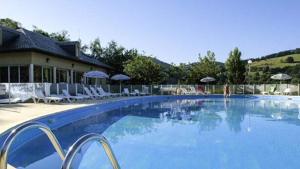 A swimming pool with lounge chairs and umbrellas, surrounded by a building with a tiled roof. - Apartment in Saint-geniez by Lot River (Saint-Geniez-d'Olt-et-d'Aubrac)