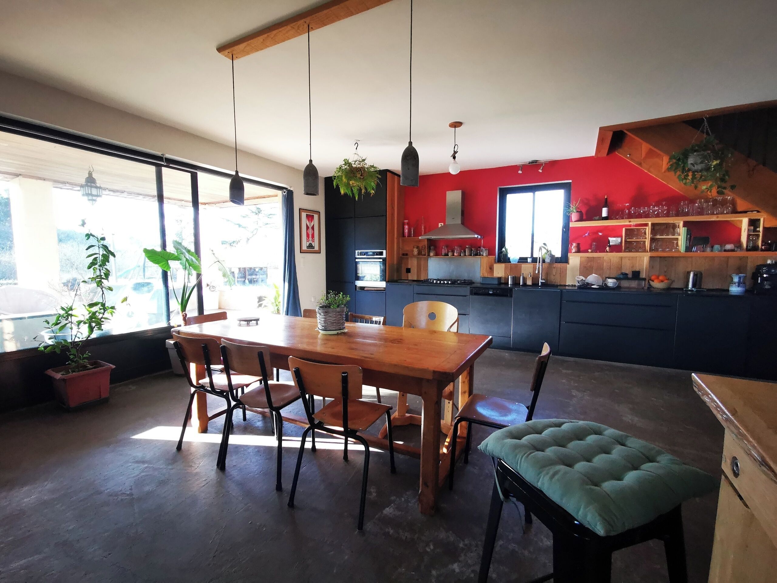 A modern kitchen with a wooden dining table and chairs, a built-in oven, and a red accent wall.