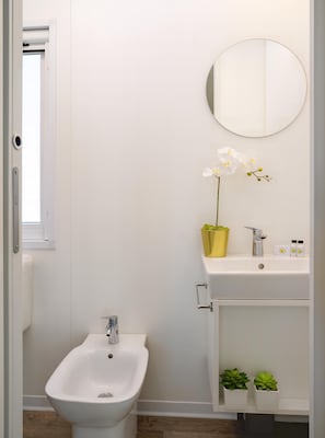 A modern bathroom with a bidet, a sink with a mirror, and two potted plants. - Friendly Mobile Home in Rimini Family Village (Rimini)