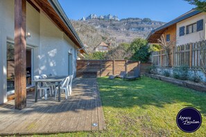 Eine Holzterrasse mit Tisch und Stühlen, ein Rasengarten und Blick auf die Berge.