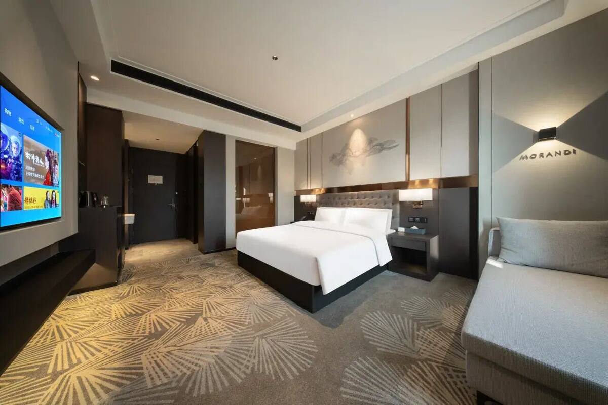 Een moderne hotelkamer met een groot bed, een bank, een televisie en een wandlamp.