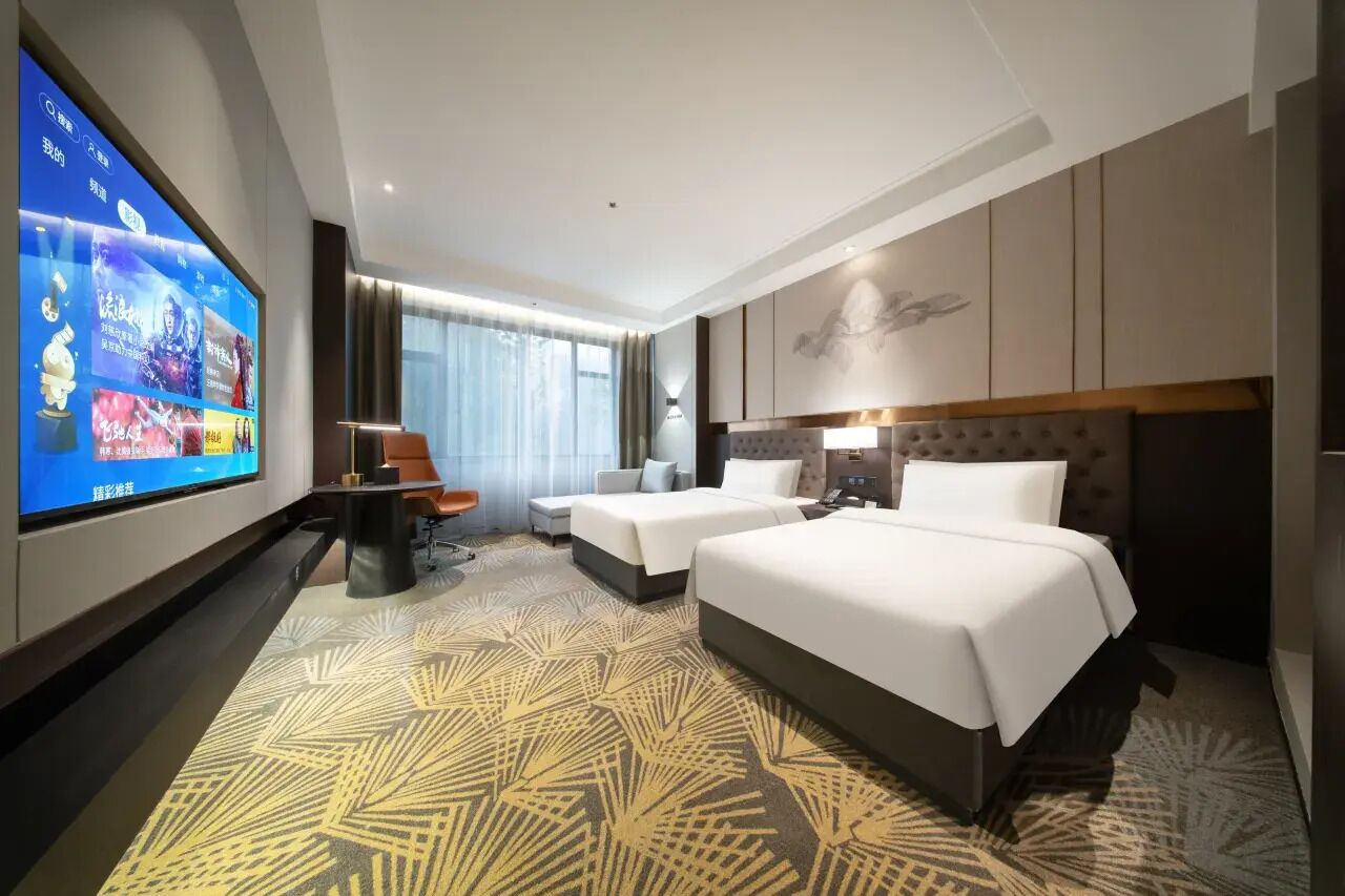 Habitació d'hotel amb un televisor gran, dos llits, un escriptori i una cadira.