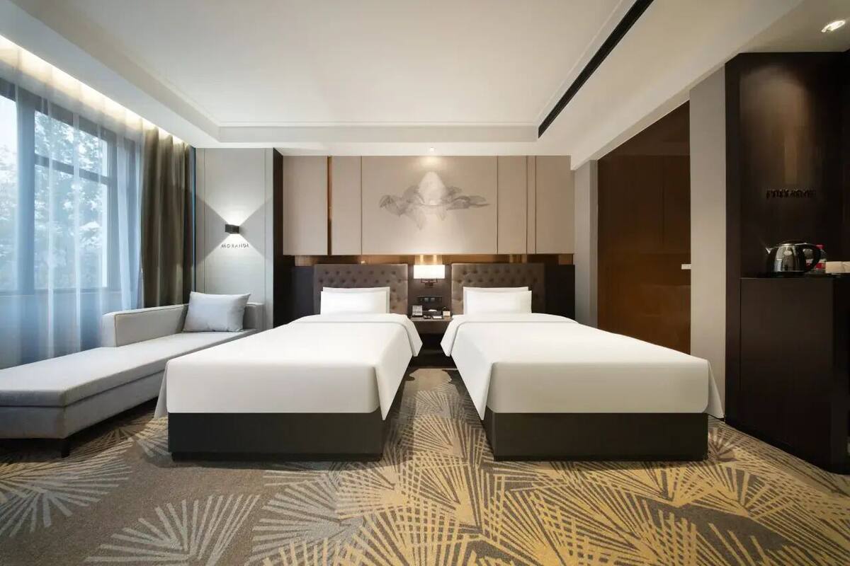 Een hotelkamer met twee bedden, een slaapbank, een tv aan de muur en een groot raam met gordijnen.