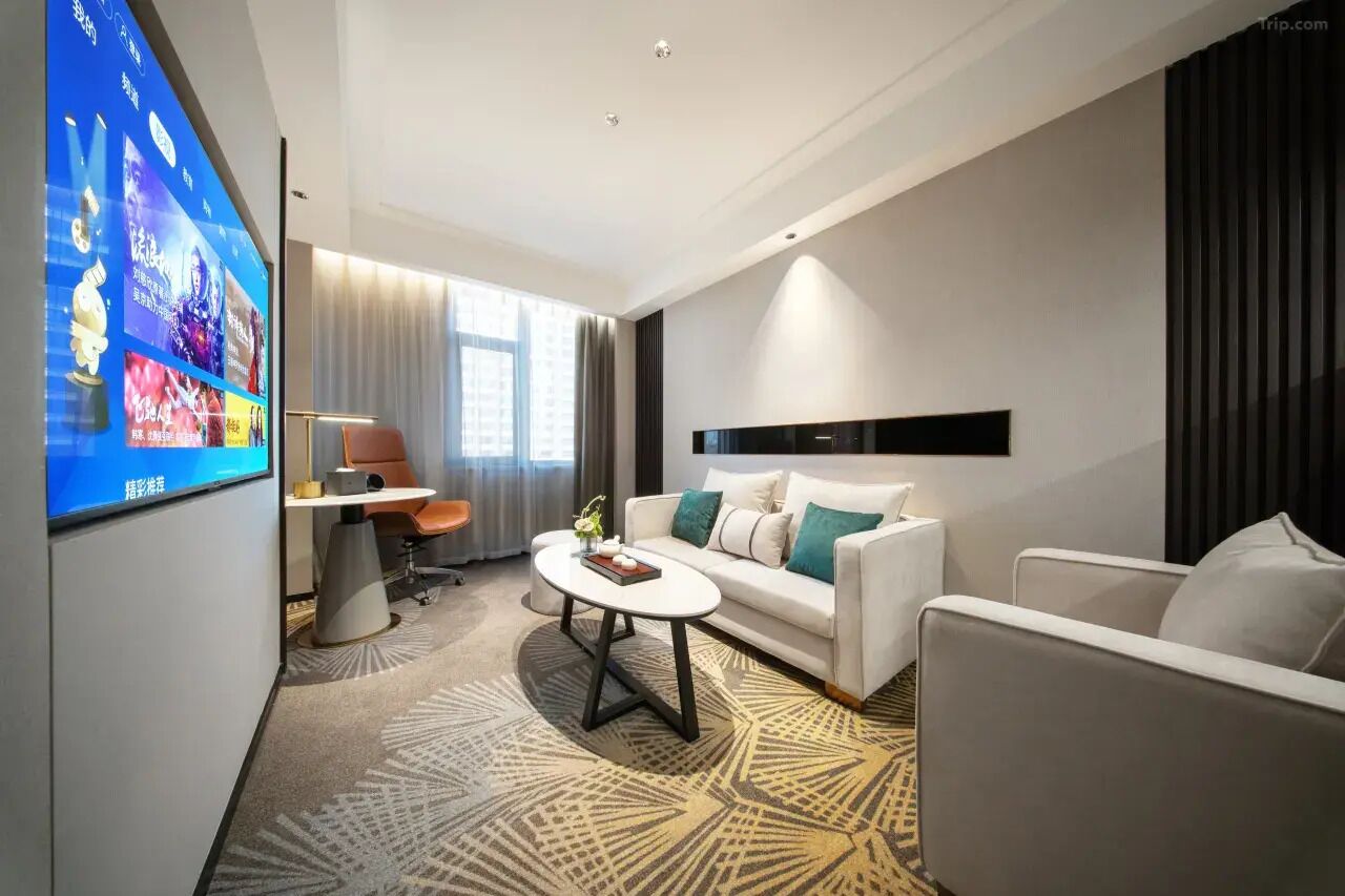 A modern hotel room with a flat-screen TV, a white sofa, a coffee table, and a desk with a chair.