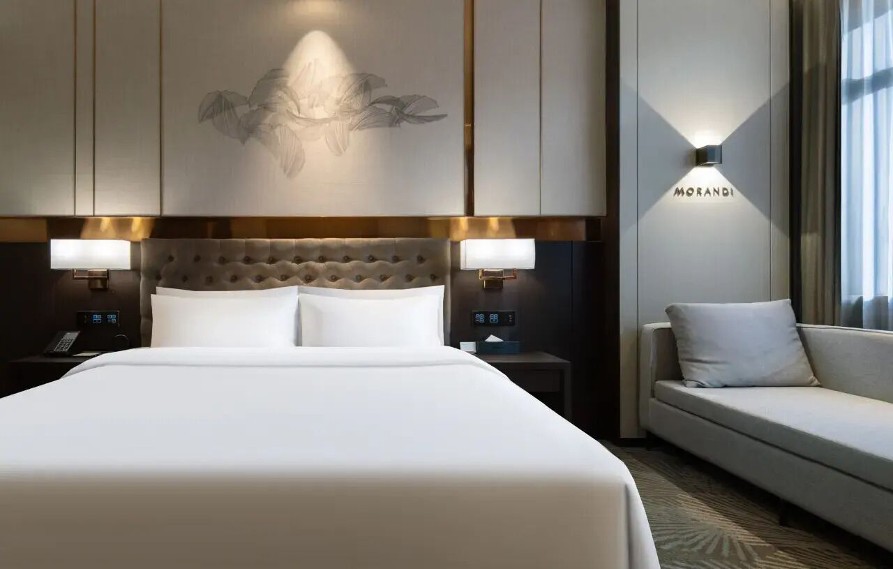 A hotel room with a large bed, two bedside tables with lamps, a sofa, and a wall-mounted light.
