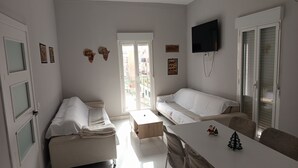 Ett modernt, väl upplyst rum med en vit soffa, ett matbord med stolar och en tv som är monterad på väggen.