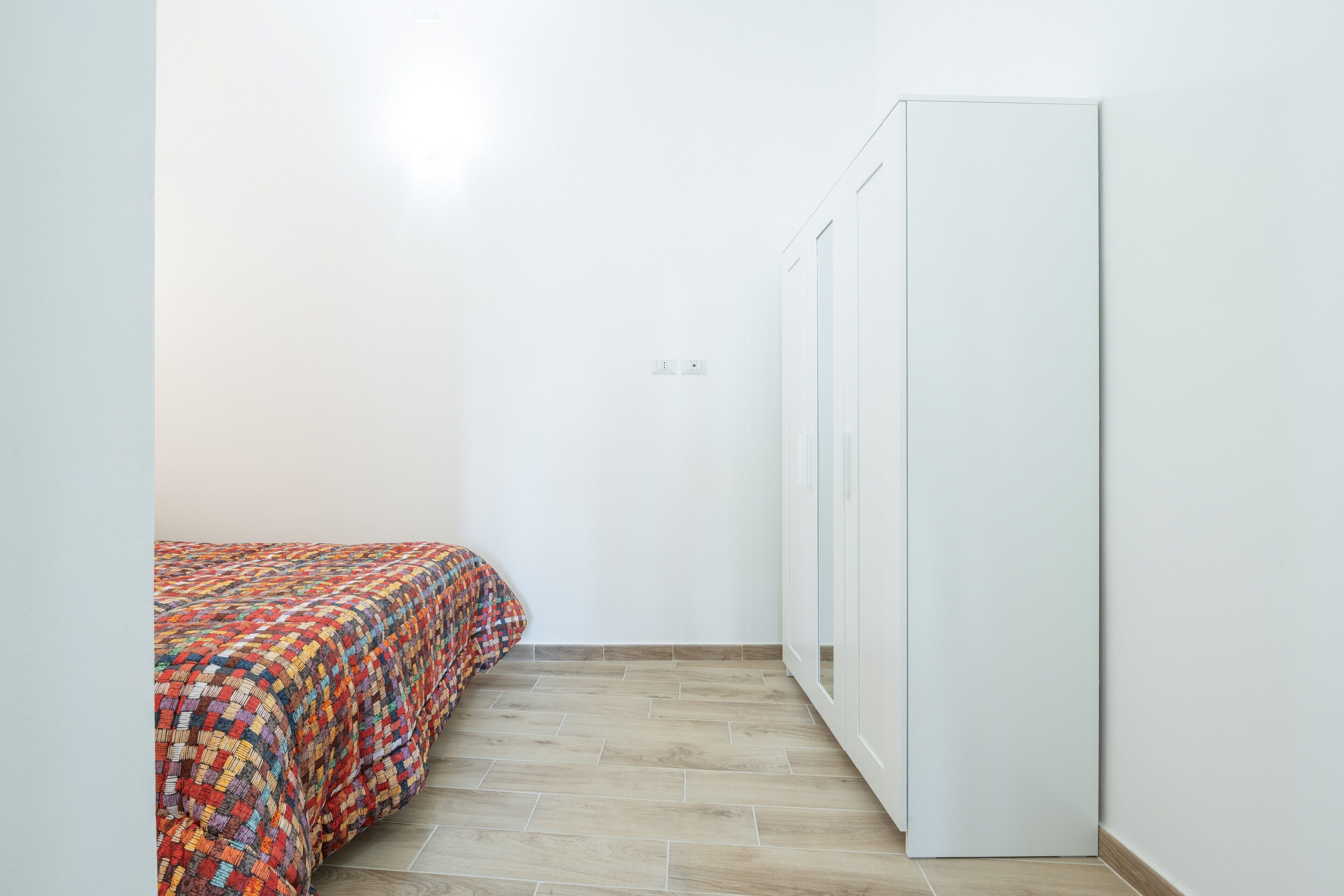 Een slaapkamer met een bed, kledingkast en een vloer van lichte tegels.