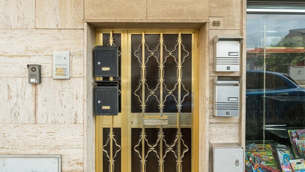 A building entrance with a metal gate, mailboxes, and a number '69' on the wall.