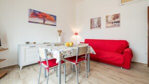 A dining area with a table, chairs, a red sofa, and wall art.