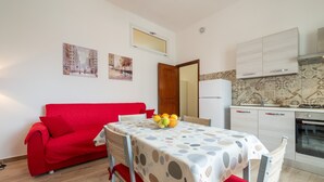 A dining area with a table set for two, a red sofa, and a kitchen with white cabinets and a tiled backsplash.