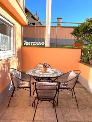 Eine Terrasse mit einem runden Tisch, vier Stühlen, einem Blumentopf und einem Schild mit der Aufschrift 'Terrasse'.