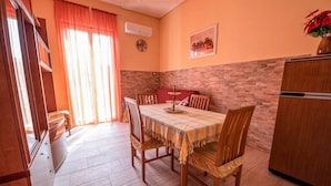 Un coin repas avec une table dressée pour quatre personnes, des chaises en bois, un canapé rouge, un comptoir de cuisine et un réfrigérateur.