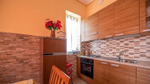 Une cuisine compacte avec des meubles de rangement en bois, un four encastré et une fenêtre avec des rideaux.