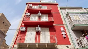 Un bâtiment rouge avec des volets et des balcons blancs, équipé de climatiseurs et portant une enseigne indiquant qu’il s’agit d’un centre médical.