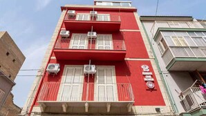 Ein rotes Gebäude mit weißen Fensterläden und Balkonen, inklusive Klimaanlagen sowie einem Schild, das ein medizinisches Zentrum kennzeichnet.