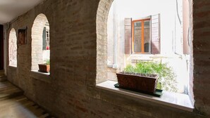 Um corredor com janelas em arco, parede de tijolos e uma janela com planta em vaso.