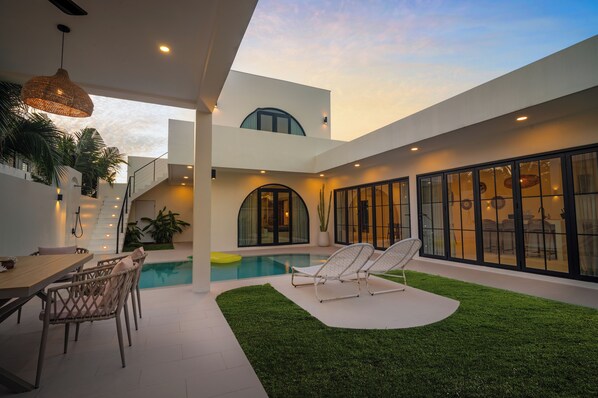 Una casa moderna con piscina, mobiliario exterior y una escalera que conduce a un nivel superior.