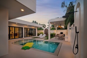 Uma área moderna de piscina interna com piscina envidraçada, espreguiçadeiras e um espaço de refeições com mesas ao ar livre.