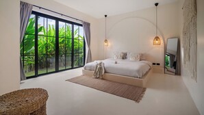 Ein Schlafzimmer mit großem Fenster, einem Bett, einer Pendelleuchte und einem Korbstuhl.