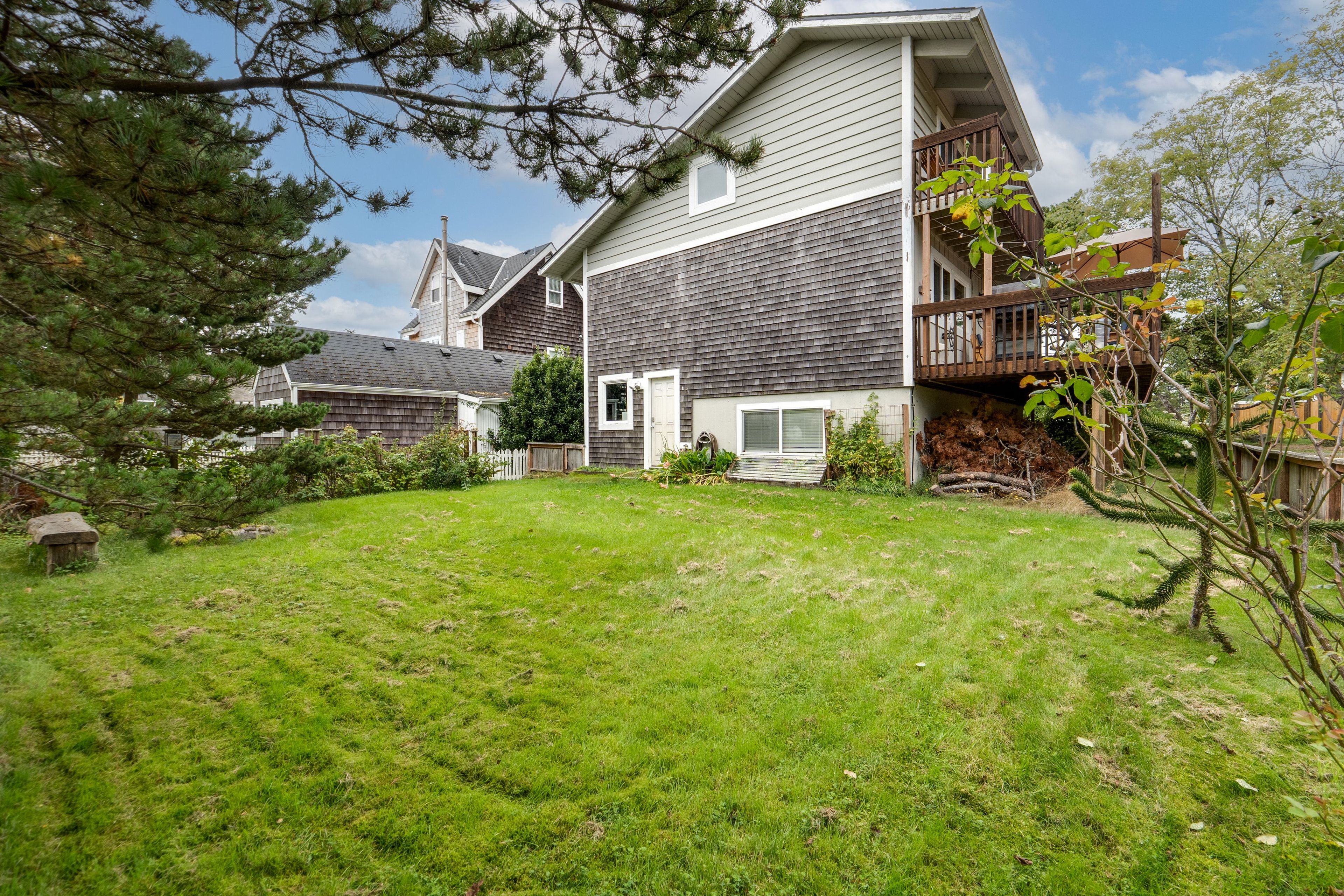 A residential property with a well-maintained lawn, a wooden deck, and a two-story house with a visible garage.